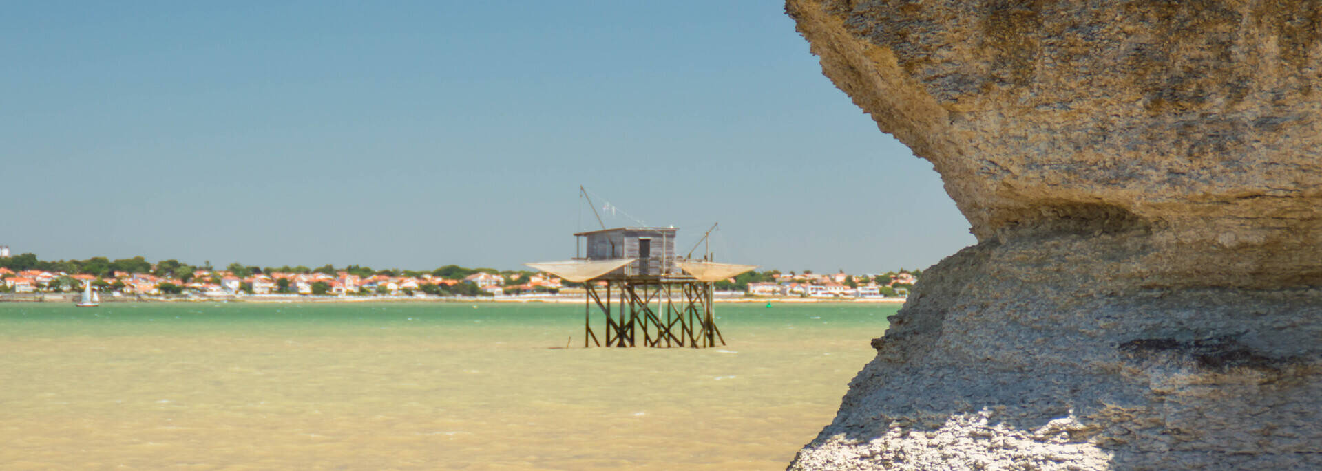 Panorama composé de roches, d'eau translucide, de ciel bleu et de carrelets
